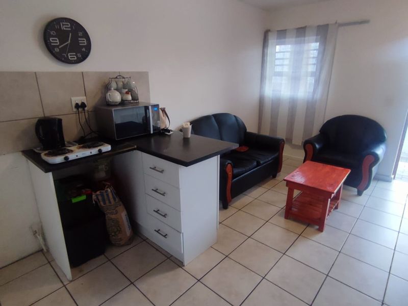 Compact open-plan living area featuring tiled flooring and a functional kitchenette with built-in cabinetry and countertop space.