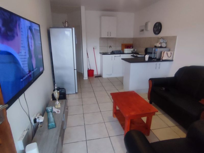Open plan living area featuring a compact kitchen with built-in cabinetry and tiled flooring throughout the combined lounge and kitchen space.