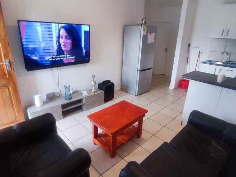 Open plan living area featuring tiled flooring and a compact kitchen with built-in cabinetry and a breakfast counter.