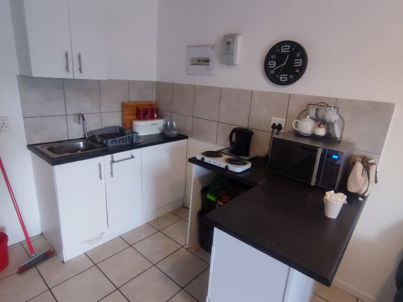 Compact kitchen featuring white cabinetry, dark laminate countertops, tiled backsplash, and tiled flooring, providing a functional workspace for an apartment.