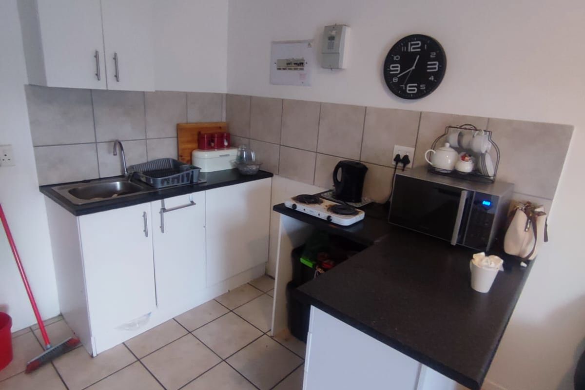 Compact kitchen featuring white cabinetry, dark laminate countertops, tiled backsplash, and tiled flooring, providing a functional workspace for an apartment.