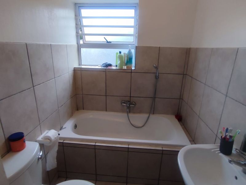 A functional bathroom featuring a bathtub with handheld shower, pedestal basin, toilet, and neutral ceramic tiling throughout.