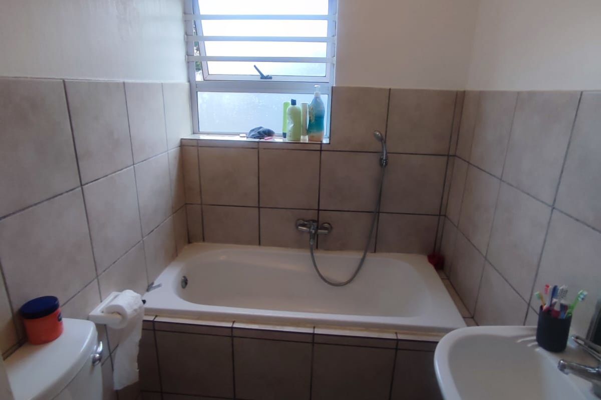 A functional bathroom featuring a bathtub with handheld shower, pedestal basin, toilet, and neutral ceramic tiling throughout.