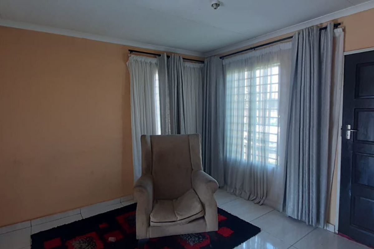 A living room featuring tiled flooring, large windows with security bars, and a dark panelled entrance door.