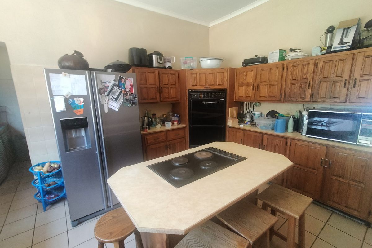 A functional kitchen featuring traditional wooden cabinetry, a central island with a built-in electric cooktop, and tiled flooring.