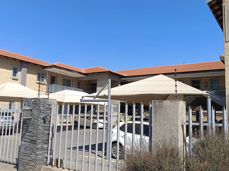 Exterior view of the apartment complex featuring a paved parking area with shade cloth carports, secured by steel palisade fencing and electric security wires.