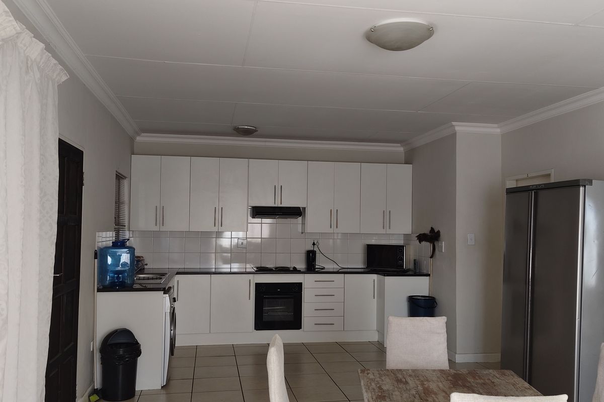 A functional kitchen featuring white built-in cabinetry, tiled backsplash, integrated oven, extractor fan, and tiled flooring in an open-plan layout.