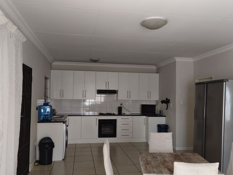 A functional kitchen featuring white built-in cabinetry, tiled backsplash, integrated oven, extractor fan, and tiled flooring in an open-plan layout.