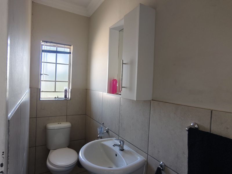 A functional bathroom featuring a pedestal basin, toilet, and wall-mounted medicine cabinet with neutral wall tiling and a window for natural light.