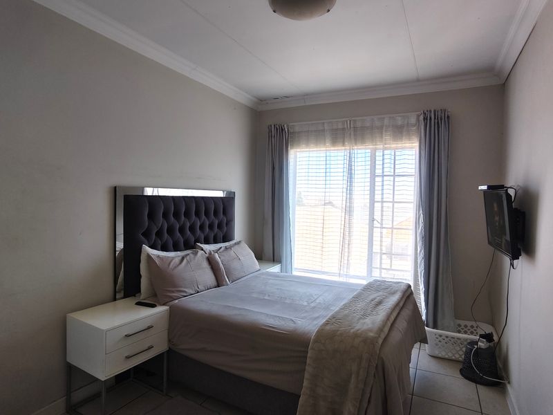 A functional bedroom featuring tiled flooring, a sliding glass door providing natural light, and neutral wall finishes.