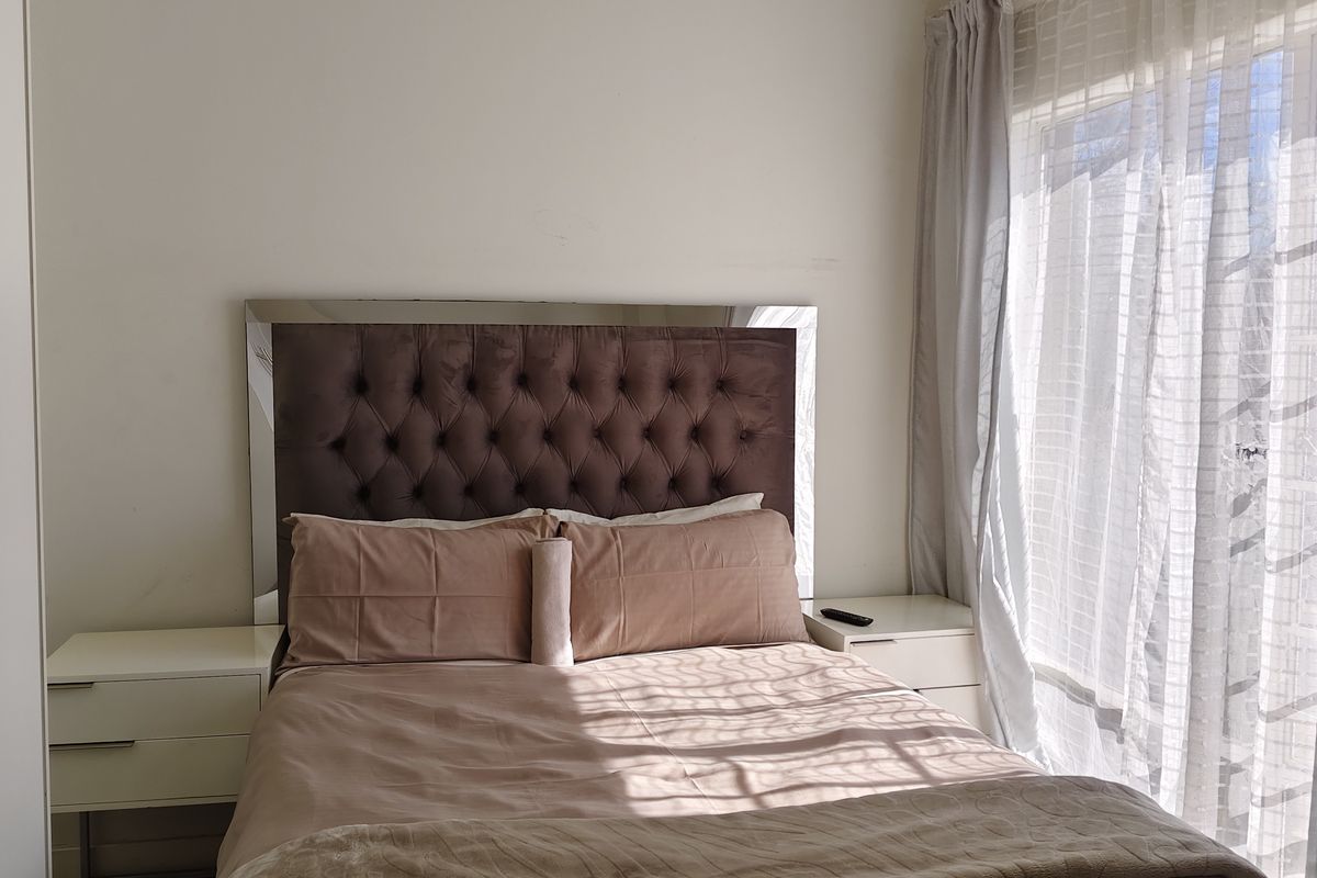 A bedroom featuring tiled flooring, built-in cupboards, and natural light through a large window with sheer curtains.