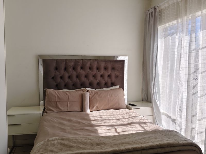 A bedroom featuring tiled flooring, built-in cupboards, and natural light through a large window with sheer curtains.
