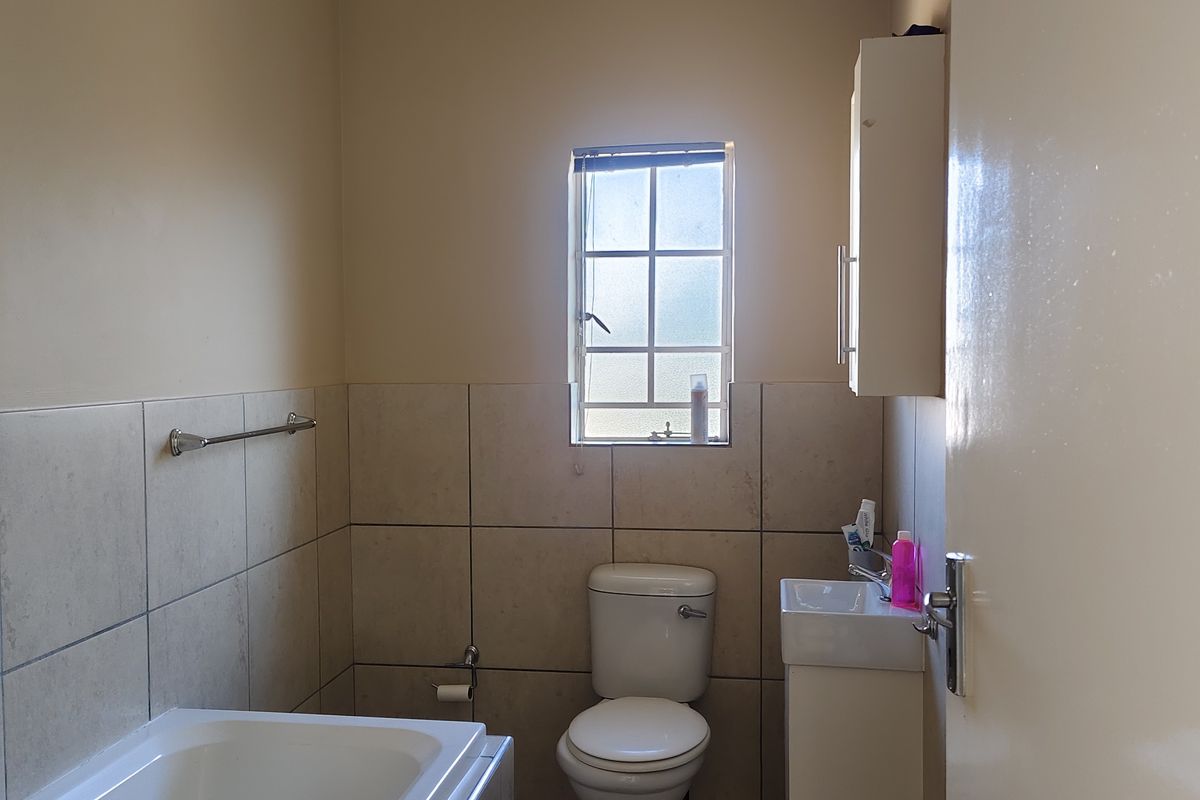 A functional bathroom featuring a bathtub, toilet, and vanity basin with wall-mounted storage, finished with neutral wall and floor tiling.