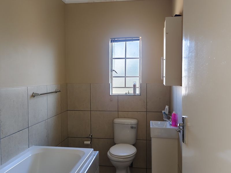 A functional bathroom featuring a bathtub, toilet, and vanity basin with wall-mounted storage, finished with neutral wall and floor tiling.