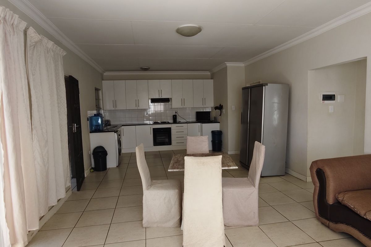Open-plan living and kitchen area featuring tiled flooring, white built-in cabinetry, and integrated kitchen appliances.