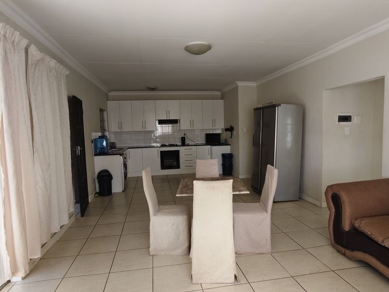 Open-plan living and kitchen area featuring tiled flooring, white built-in cabinetry, and integrated kitchen appliances.