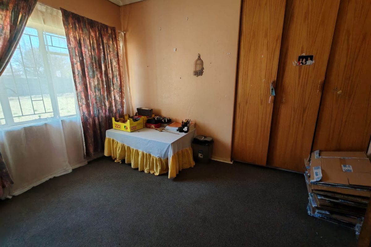 A bedroom featuring built-in wooden cupboards and a steel-framed window, requiring cosmetic updates to the walls and flooring to improve its overall condition.