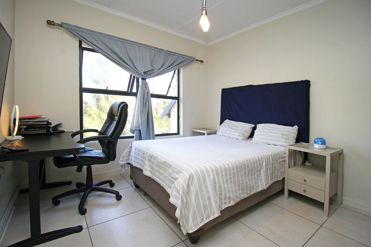 A functional bedroom featuring tiled flooring, a large window providing natural light, and neutral wall finishes.