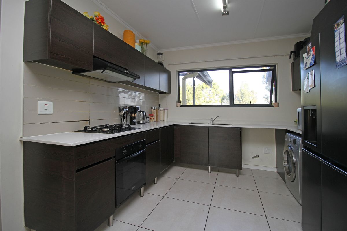 A functional kitchen featuring dark wood-finish cabinetry, a built-in gas hob, extractor fan, oven, and tiled flooring with a double sink.