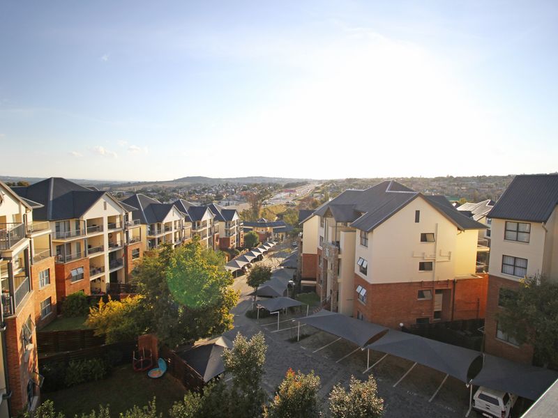 An elevated aerial view of a modern apartment complex featuring multi-story brick and plaster buildings, covered parking bays, and landscaped grounds.