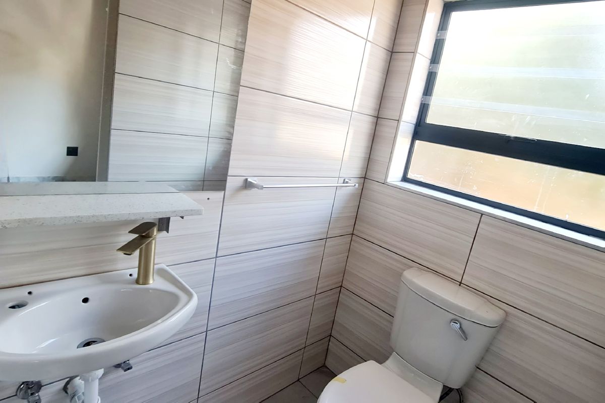 Modern bathroom featuring floor-to-ceiling neutral wall tiles, a wall-mounted basin with gold-tone faucet, a built-in mirror, and a standard toilet.
