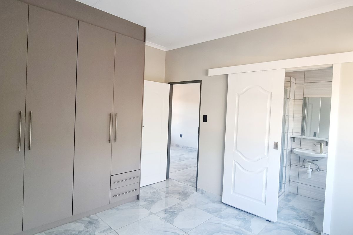 A modern bedroom featuring built-in cupboards, marble-look floor tiles, and a sliding door leading to an en-suite bathroom.