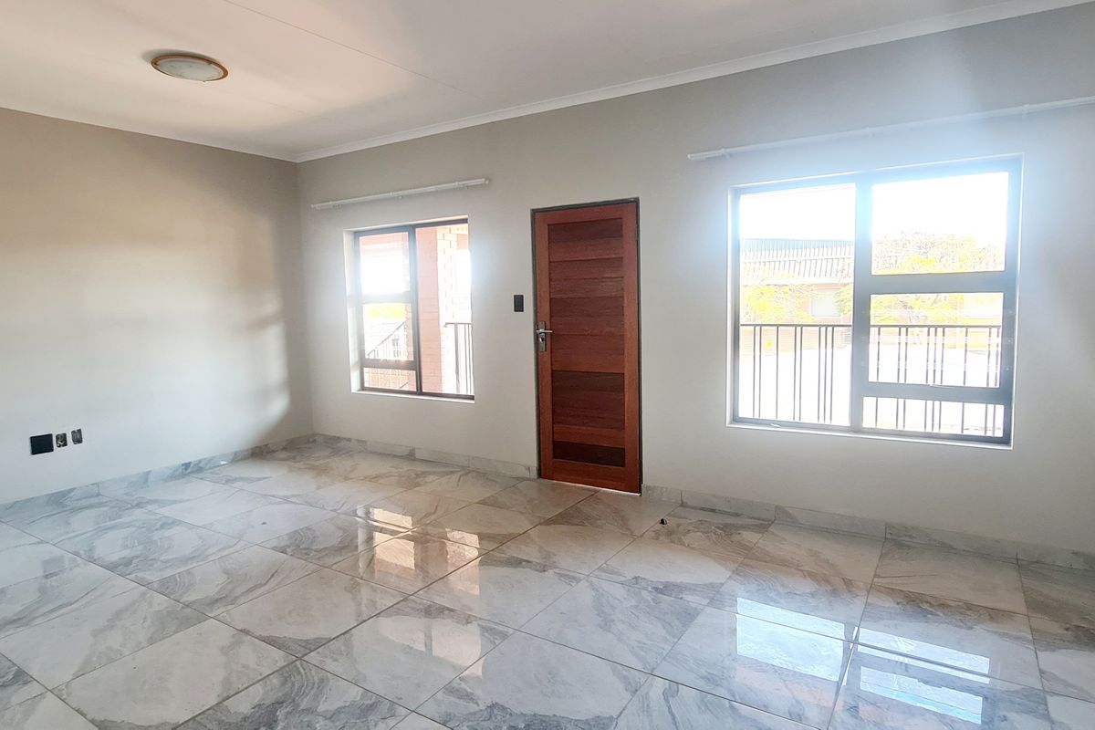 A bright, open-plan living area featuring modern marble-look floor tiles, neutral wall finishes, and large windows providing ample natural light.
