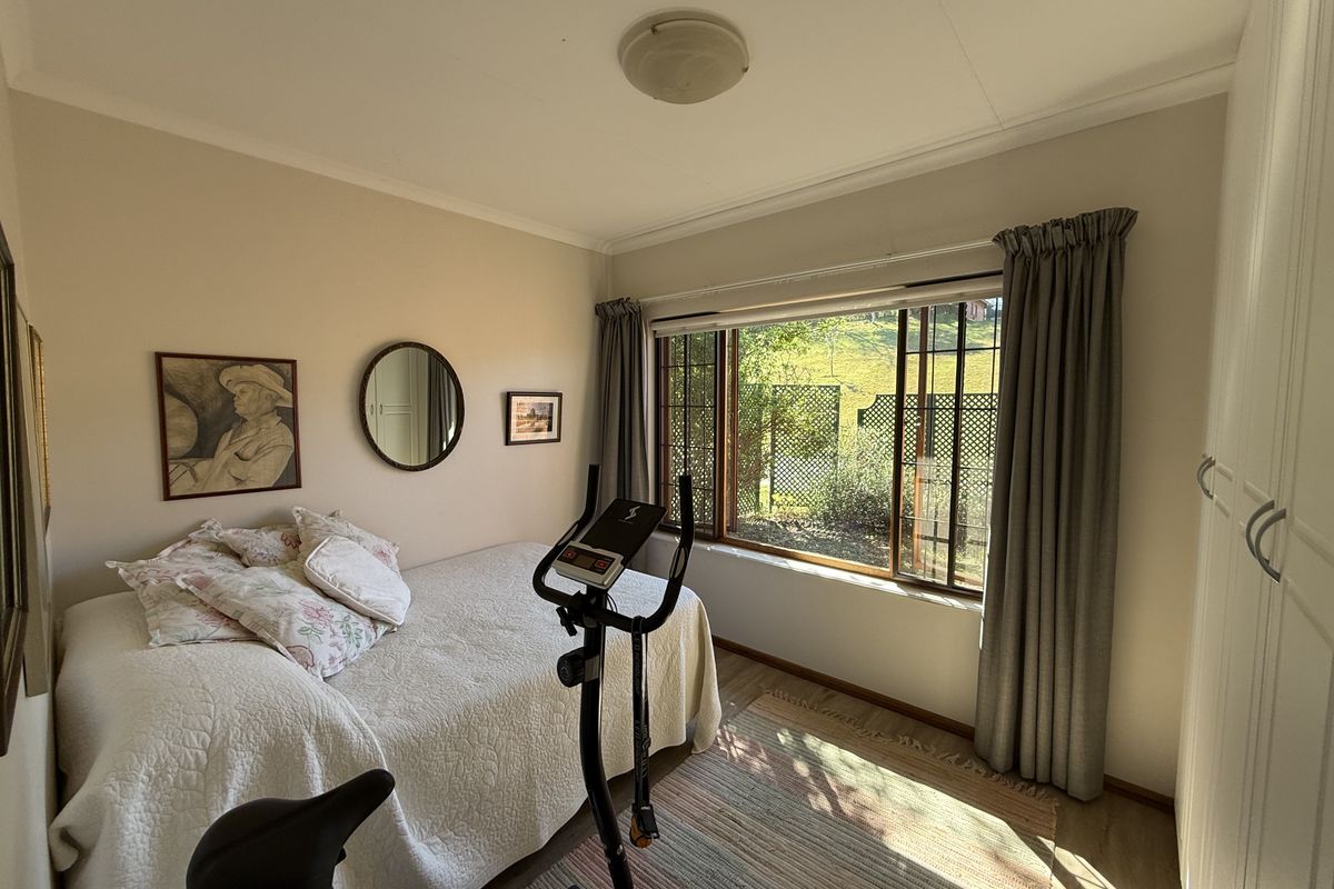 A bedroom featuring built-in wardrobes, large windows with garden views, and neutral wall finishes.