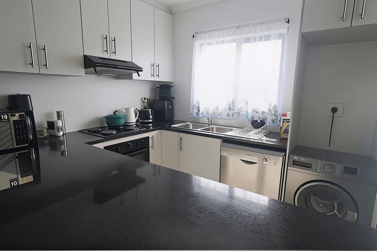 Modern kitchen featuring sleek white cabinetry, contrasting black granite countertops, integrated dishwasher, and dedicated space for laundry appliances.