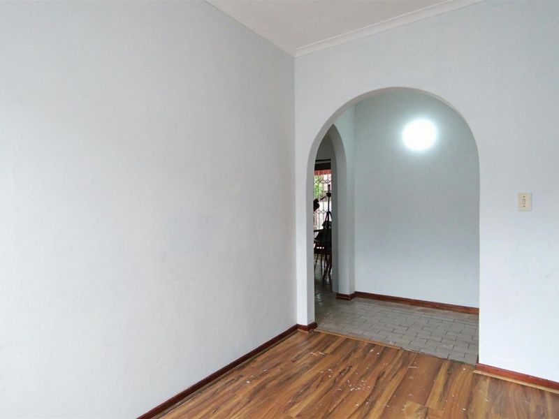 An empty living area featuring laminate flooring, a decorative archway leading to an adjacent space, and coved ceiling detailing.