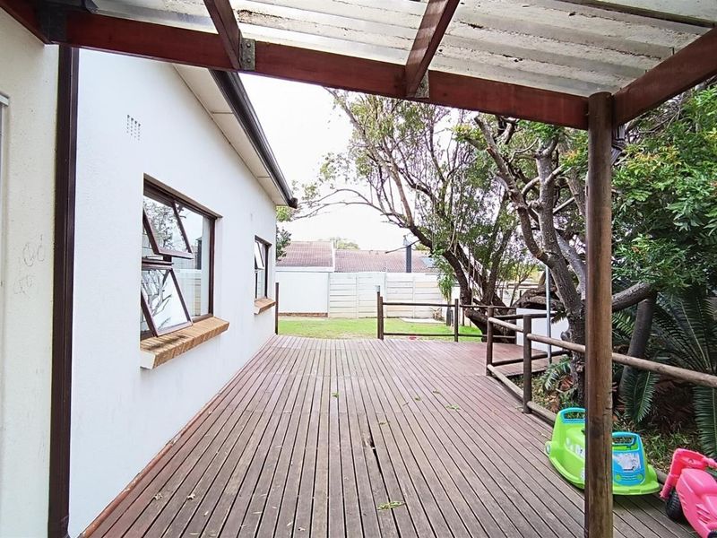 A covered timber deck patio area featuring a translucent roof, providing access to the rear garden space.