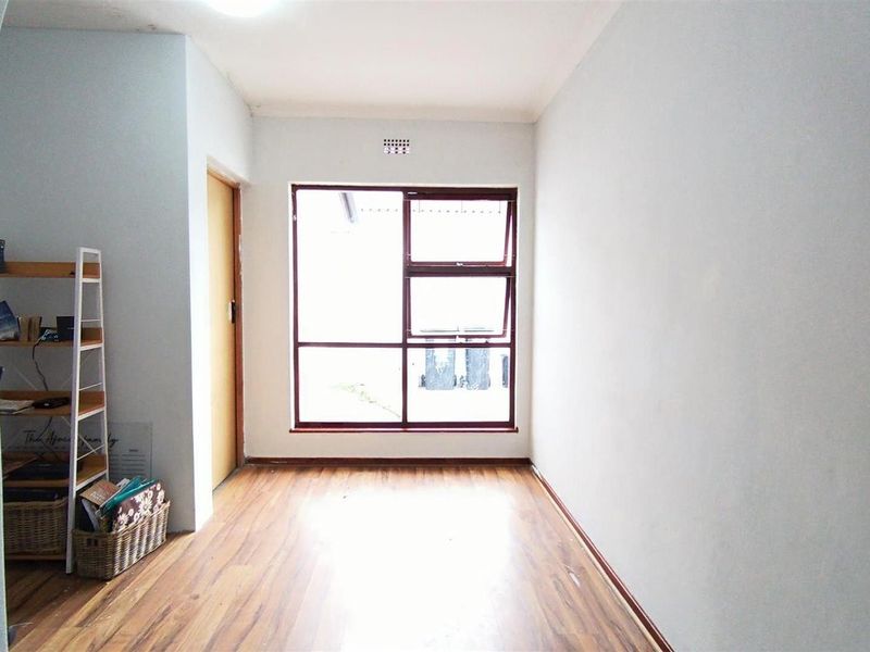 A bright, empty bedroom featuring laminate flooring, neutral walls, and a large window providing natural light.