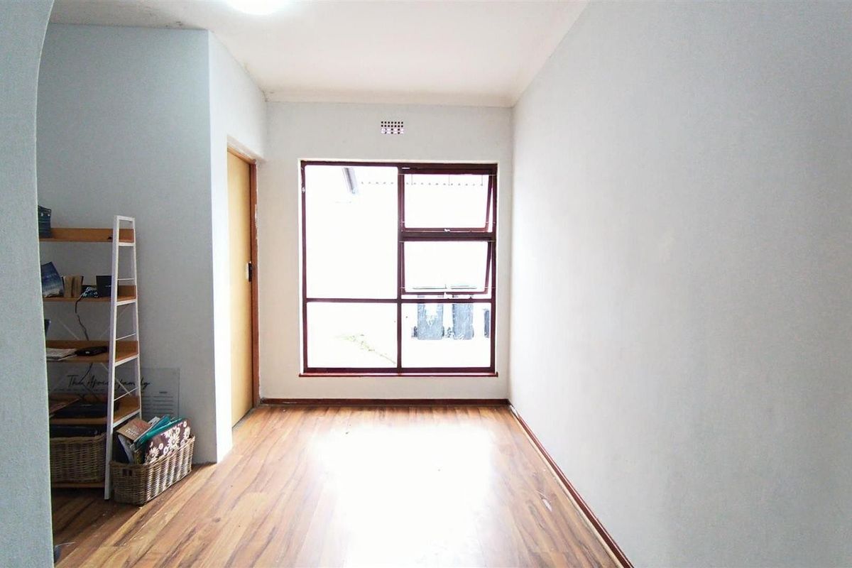 A bright, empty bedroom featuring laminate flooring, neutral walls, and a large window providing natural light.
