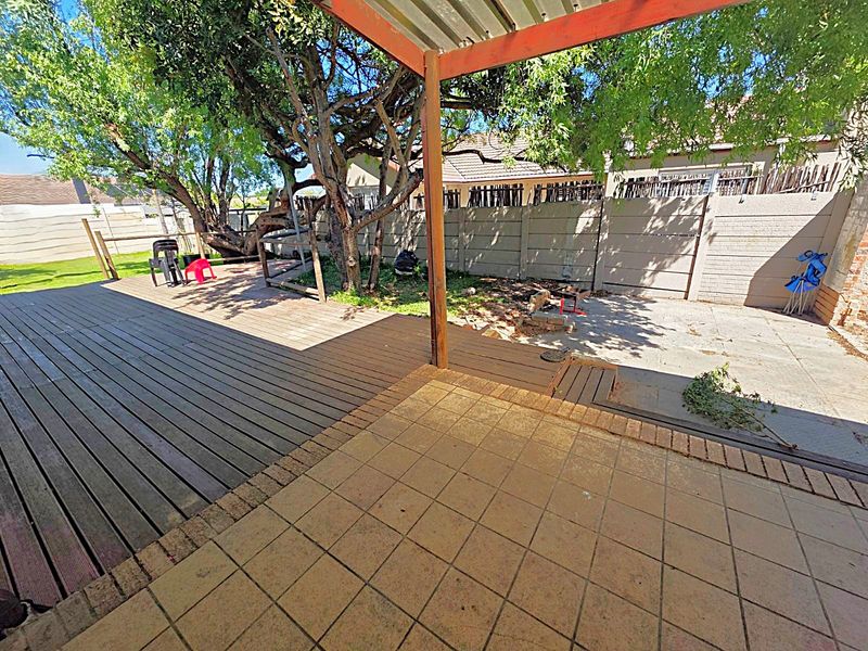 Outdoor patio area featuring a combination of timber decking and tiled flooring, shaded by a pergola and mature trees in the rear garden.