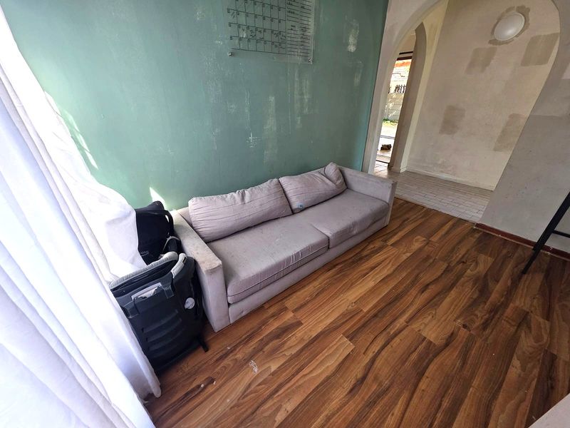 Living room featuring wood-look laminate flooring and an arched entryway, currently requiring wall repairs and fresh paint to improve the overall aesthetic.