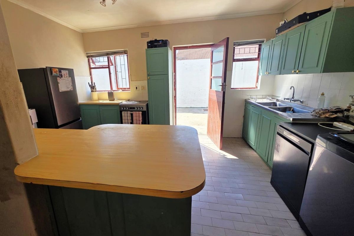 A functional kitchen featuring built-in cabinetry, a double basin sink, tiled flooring, and direct access to the rear exterior.