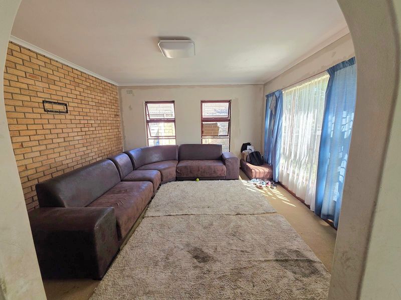 Spacious living room featuring an exposed brick wall, large windows for natural light, and carpeted flooring, offering a blank canvas for renovation.