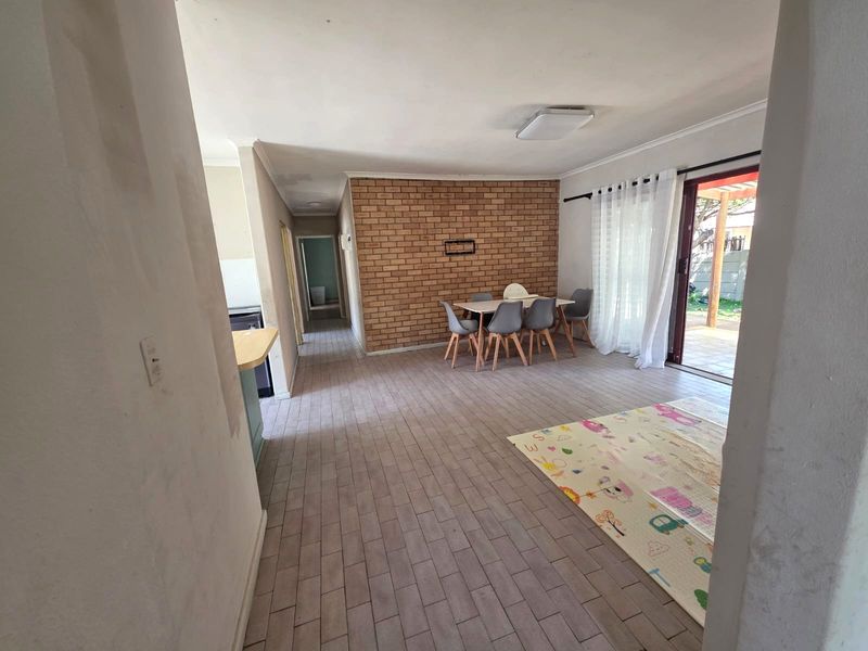 Open-plan living and dining area featuring an exposed brick wall, tiled flooring, and direct access to the outdoor patio through sliding glass doors.