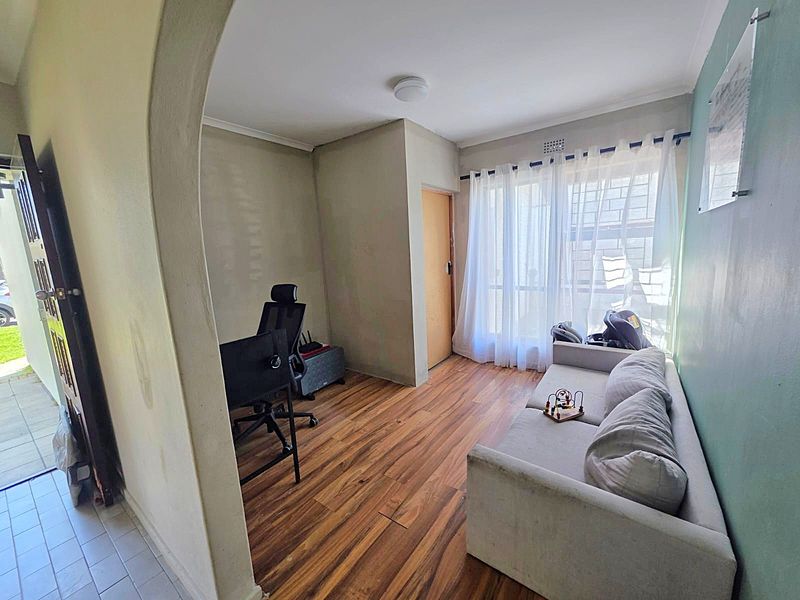 A living area featuring laminate flooring, an arched entryway, and window security bars, offering a functional space with potential for cosmetic updates.