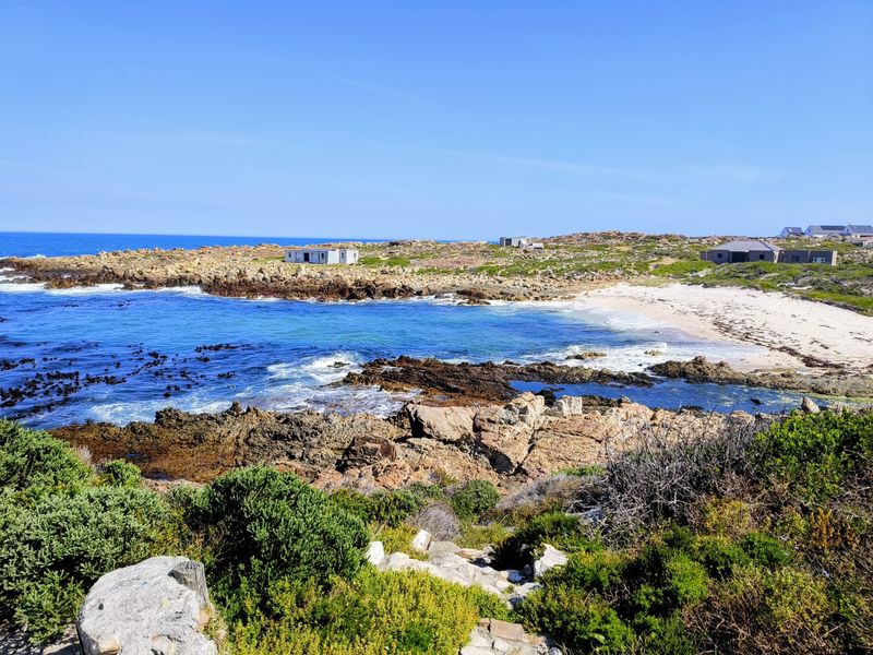 A scenic coastal view featuring a rocky shoreline, sandy beach, and clear blue ocean waters.