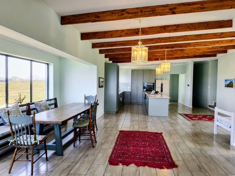 Spacious open-plan kitchen and dining area featuring exposed timber ceiling beams, modern cabinetry, a central island, and large windows with natural light.
