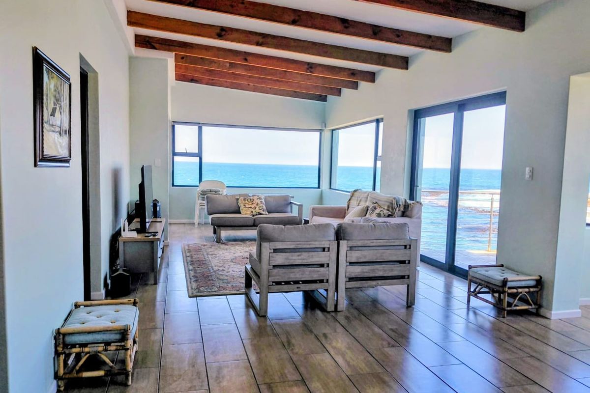 Spacious living area featuring exposed timber ceiling beams, tiled flooring, and expansive windows offering panoramic ocean views with direct access to the outdoors.