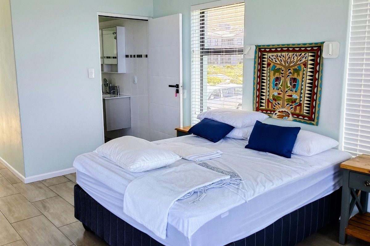 A well-maintained bedroom featuring tiled flooring, neutral wall tones, and an adjoining en-suite bathroom with natural light provided by large windows.