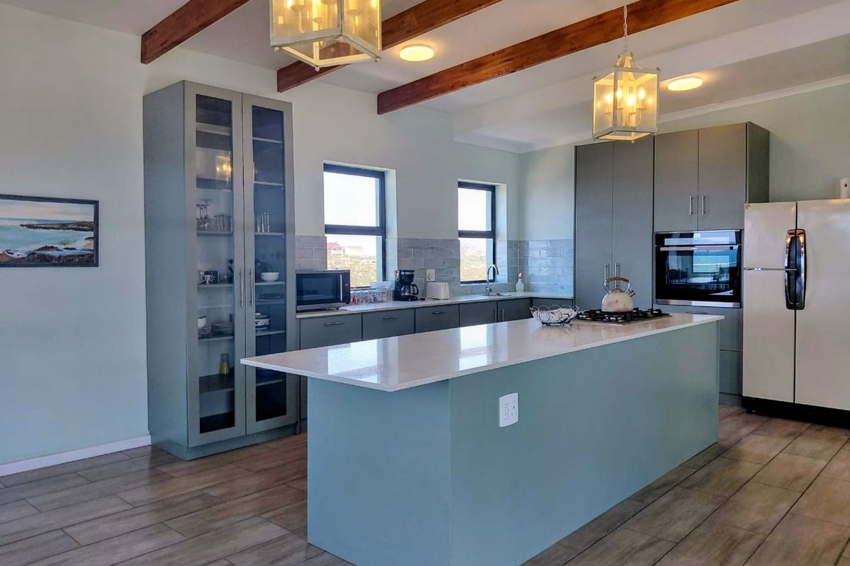 Modern kitchen featuring a central island with stone countertops, exposed timber ceiling beams, glass-fronted cabinetry, and high-quality built-in appliances.