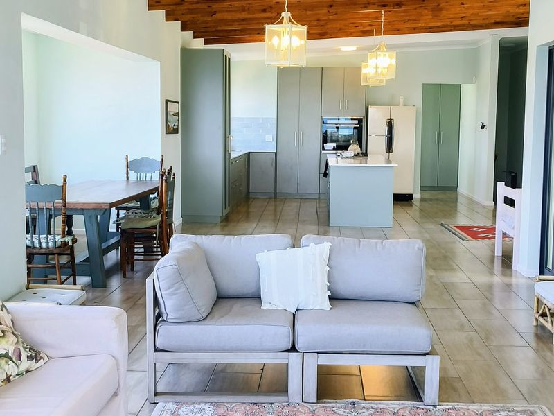 Spacious open-plan living and kitchen area featuring exposed timber ceiling beams, modern cabinetry, a central kitchen island, and neutral tiled flooring throughout.