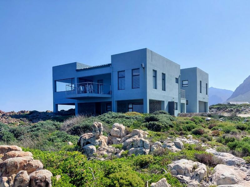 A modern multi-level coastal home featuring clean lines, large windows, and a balcony, set against a natural rocky landscape.