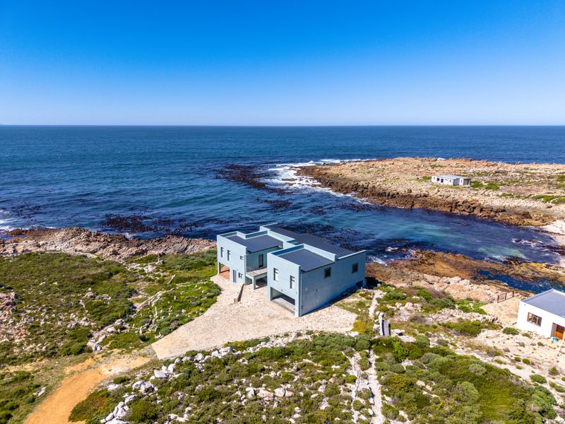 Aerial view of a modern coastal property situated on a rocky shoreline with direct ocean access and a private driveway.