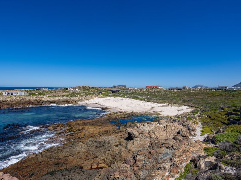 A scenic coastal view featuring a rocky shoreline, sandy beach, and clear blue ocean waters under a bright sky.