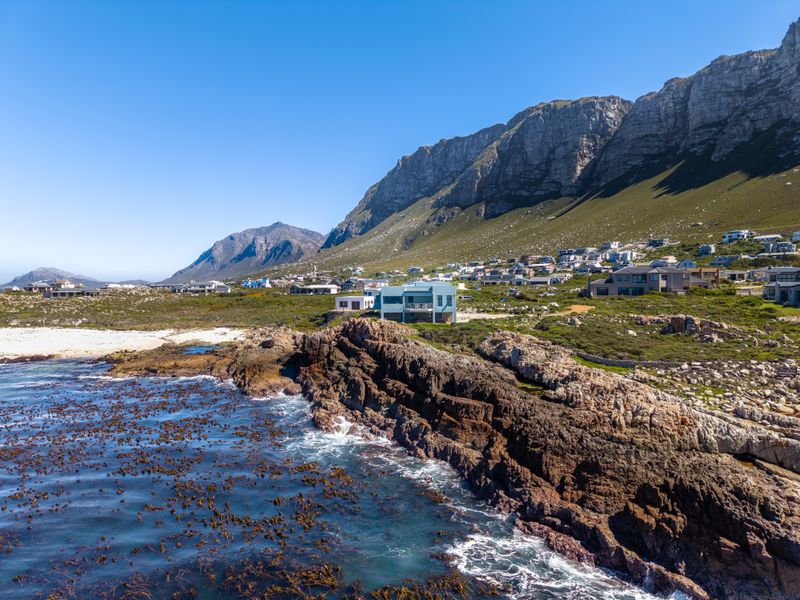 An aerial view of a coastal property situated along a rocky shoreline with a dramatic mountain range in the background.