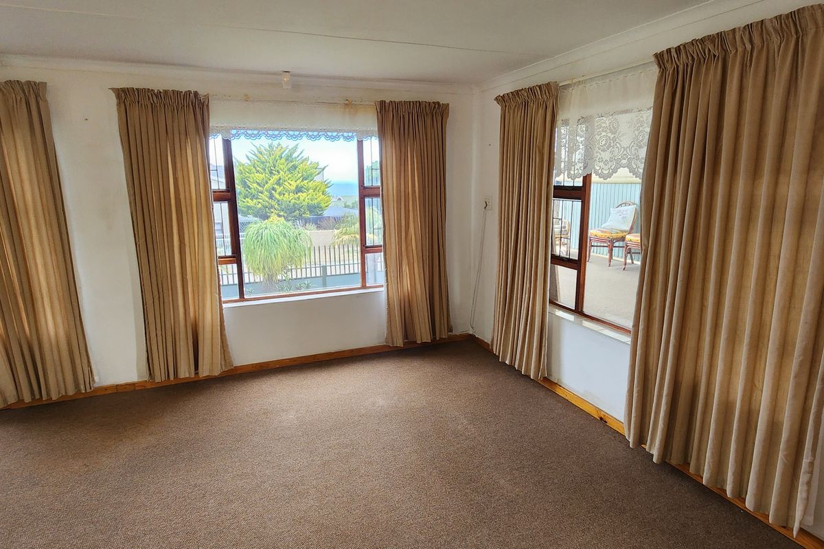 A spacious, empty living room featuring large windows with natural light, carpeted flooring, and neutral wall finishes, ready for renovation or restyling.
